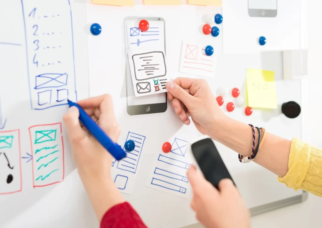 Image shows a number of hands on a whitebaord designing an interface. So what exactly is interaction design?