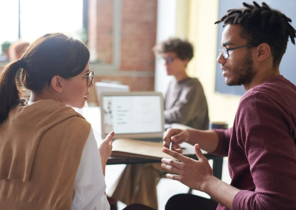 A man and a woman discuss work at a desk. Keep LinkedIn professional but still be emotive and personable.