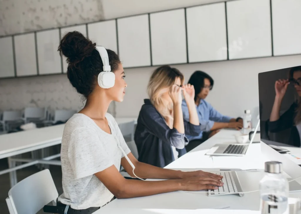 Woman works at desk with figures in the background. You need to work out your plan for using LinkedIn? Do you want to grow organically or used paid advertising?